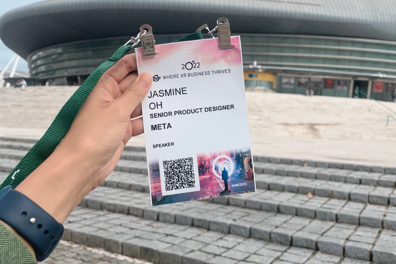 AWE EU 2022 speaker badge for Jasmine Oh, Senior Product Designer at Meta, held up outside the venue